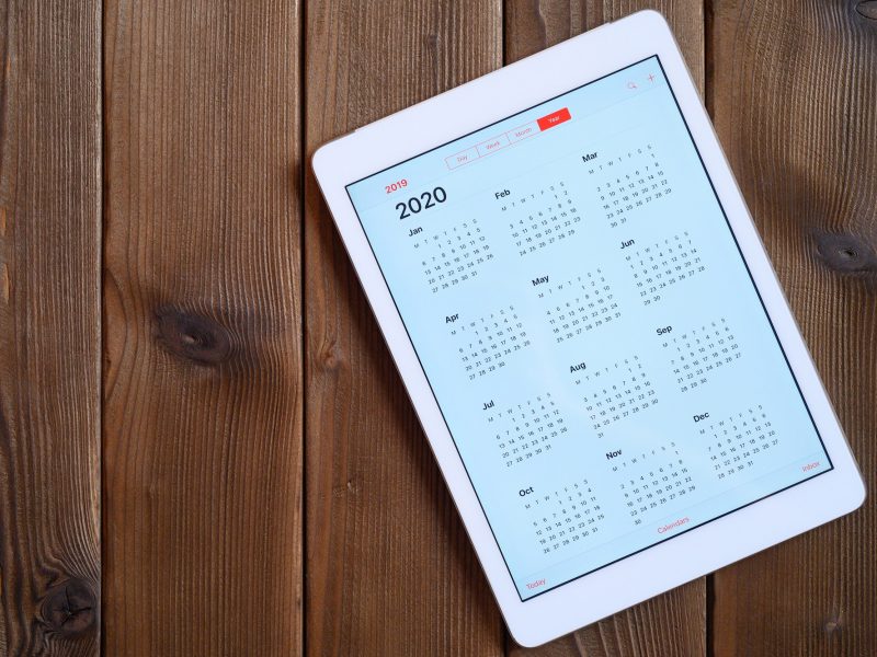 tablet with open calendar for 2020 year on a wooden background. space for text.